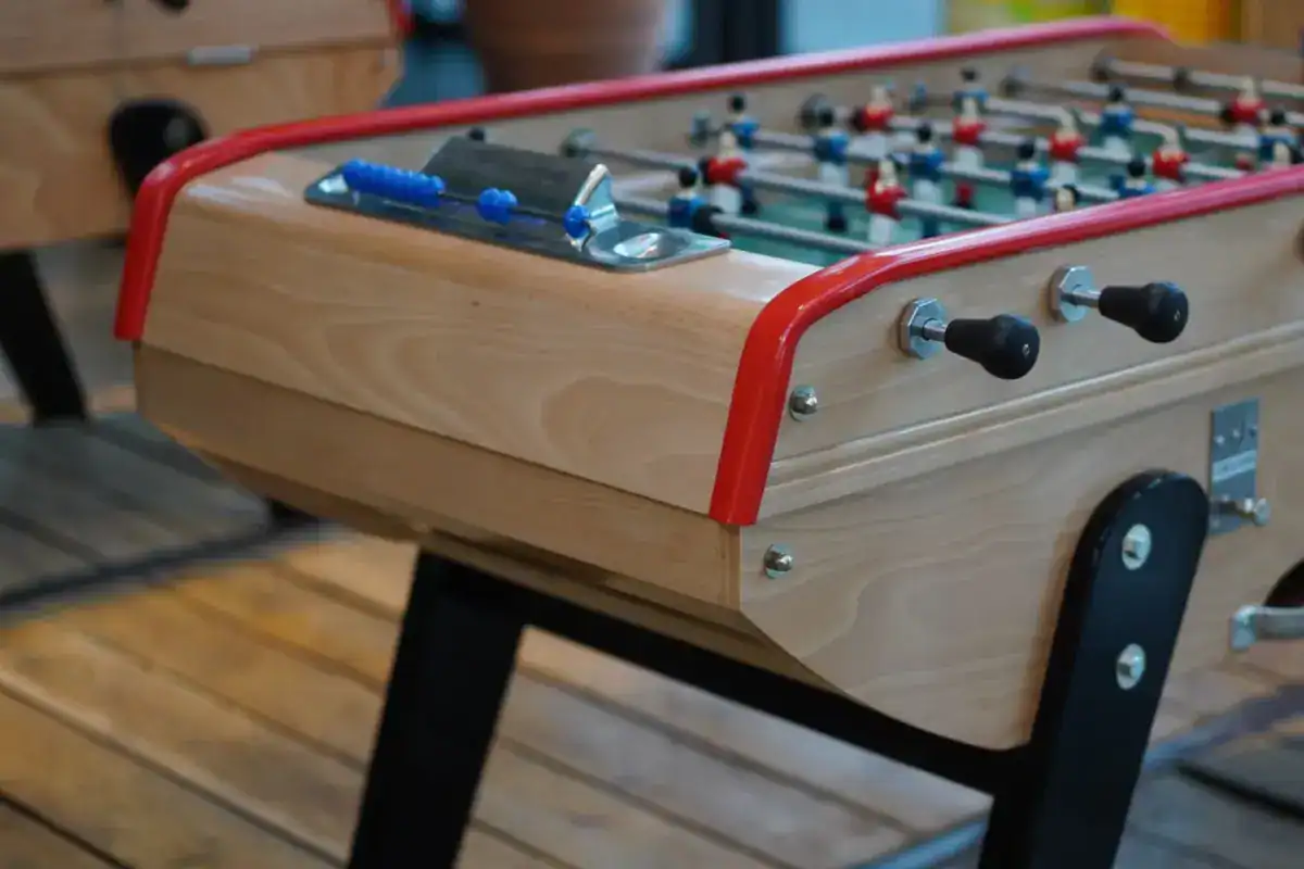 Babyfoot en bois clair à rambardes rouges, posé sur un plancher