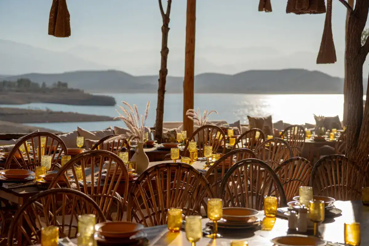 Tables dressées en terrasse au bord d’un lac, face aux montagnes, pour un déjeuner de groupe