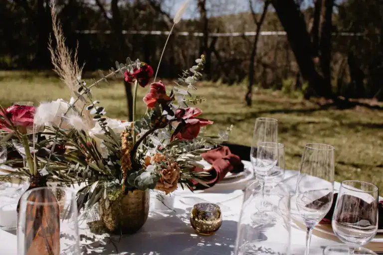 Centre de table de fleurs et de feuillages sur une table dressée en plein air