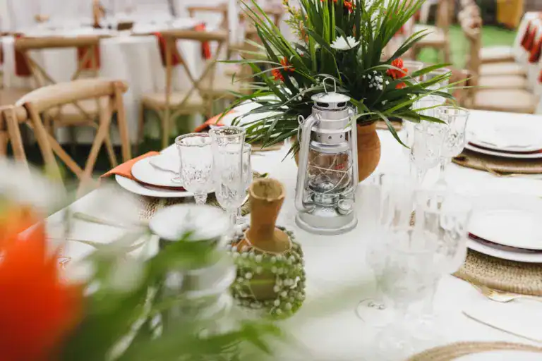 Table dressée sous un chapiteau : verres taillés, lanterne-tempête et bouquet de feuillages