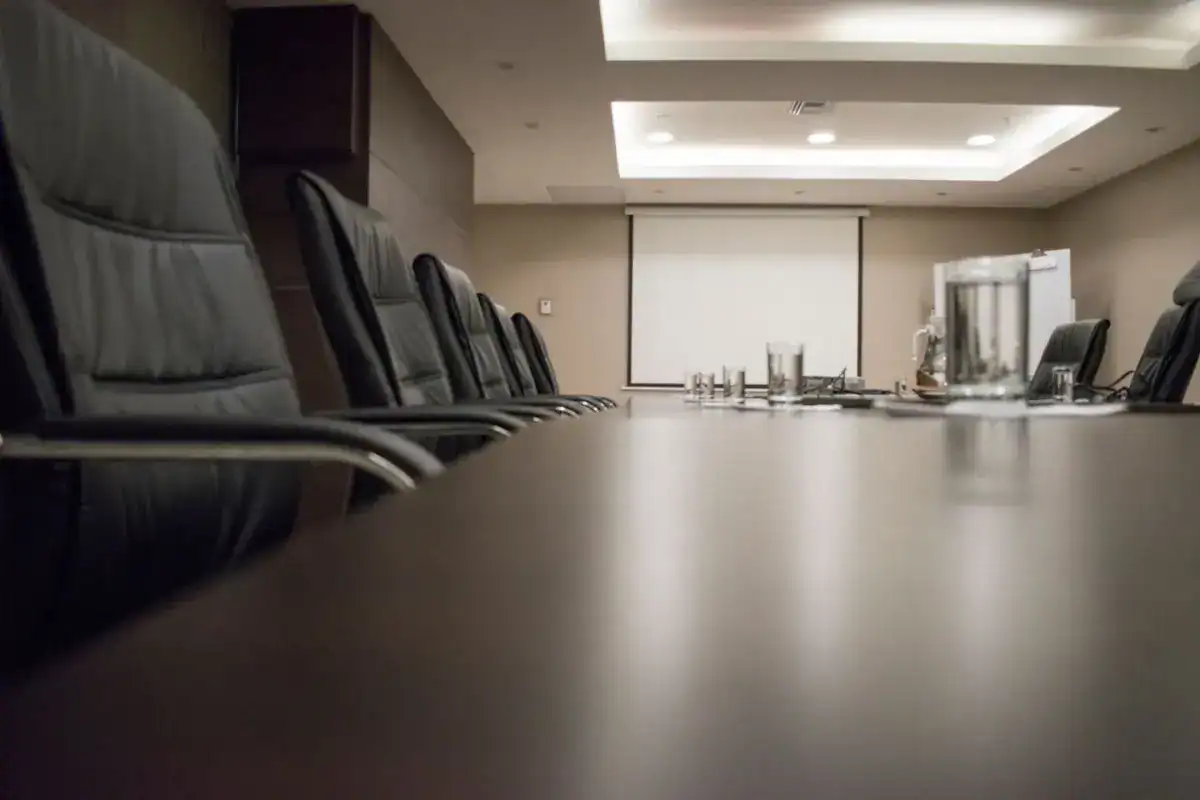 Salle de réunion vide : longue table, fauteuils noirs et écran de projection