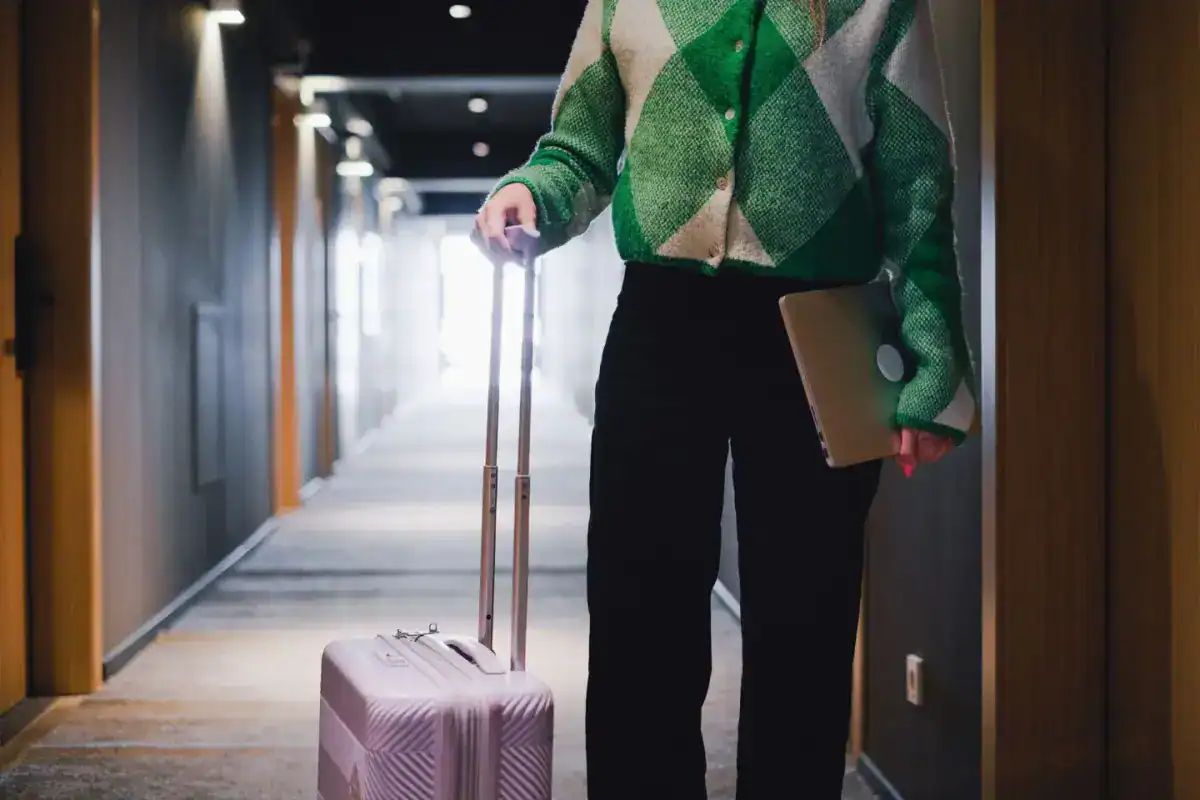 Personne de dos tirant une valise dans un couloir d’hôtel