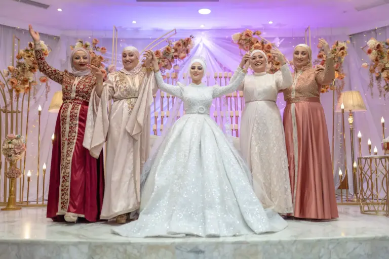 Mariée en robe blanche brodée entourée de proches en caftans sur l'estrade de la salle de réception