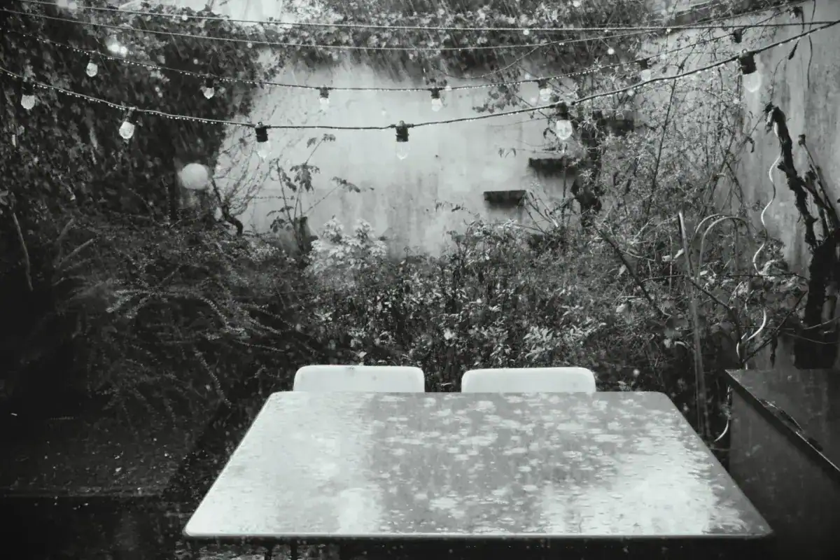 Table de jardin et guirlande d’ampoules sous une pluie battante, en noir et blanc