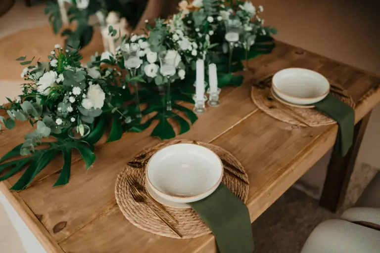 Table en bois brut dressée avec sets en fibres naturelles, vaisselle en grès et chemin de verdure