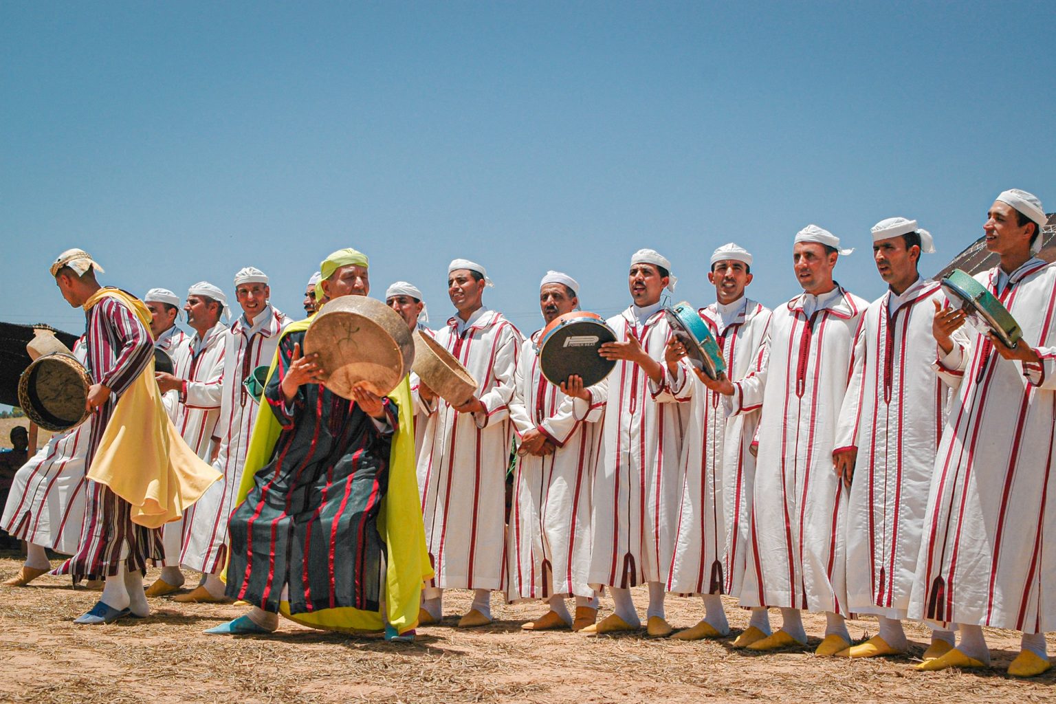 Groupe de musiciens marocains en djellaba blanche, tambours sur cadre à la main, jouant en plein air