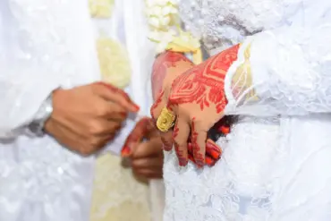 Groom slipping a ring onto the hennaed hand of a Moroccan bride