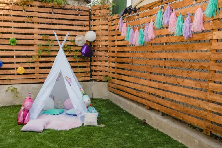 Décor d'anniversaire d'enfant dans un jardin : tipi, coussins et guirlande de pompons