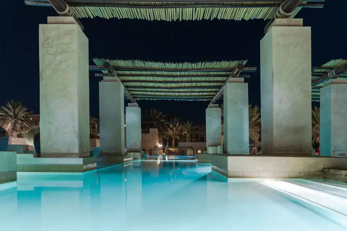 Piscine d’un hôtel de luxe éclairée la nuit, entre colonnes et palmiers