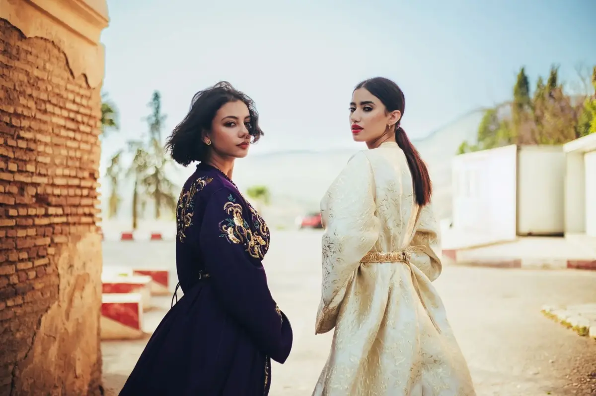 Two women wearing embroidered Moroccan caftans, one navy and one ivory