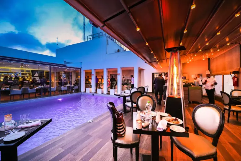 Terrasse de restaurant privatisée au bord d'une piscine, tables dressées à la tombée du jour