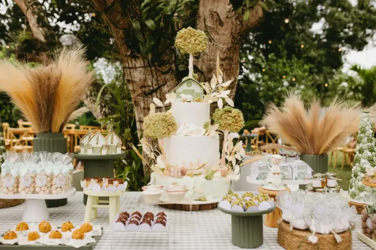 Table de fête dressée en extérieur avec gâteau à étages, douceurs et herbes de la pampa