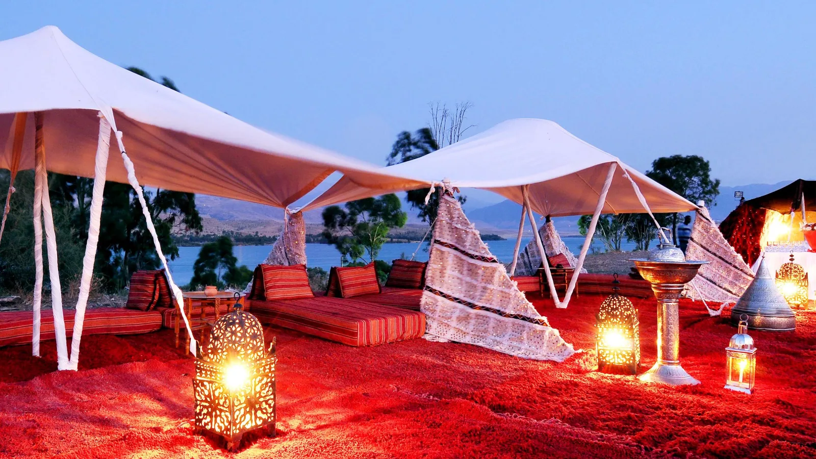 Berber lounge under white tents, red rugs and lanterns lit at dusk