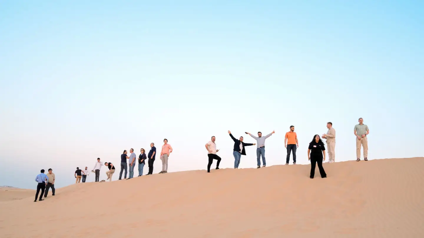 A team lined up on top of a dune, arms raised