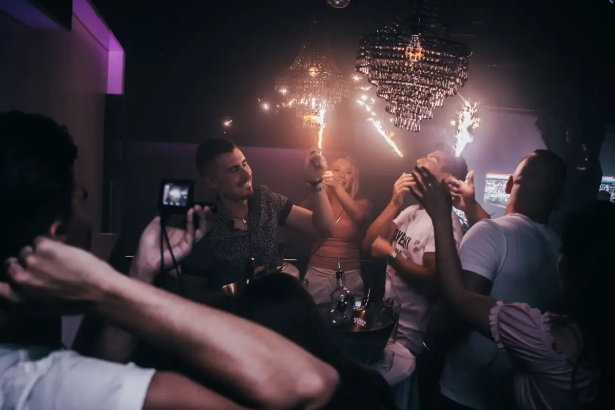 Amis fêtant un anniversaire en boîte de nuit, bouteilles à étincelles sous les lustres