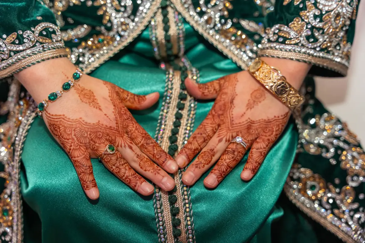 Mains ornées de henné et bague de fiançailles sur un caftan vert brodé