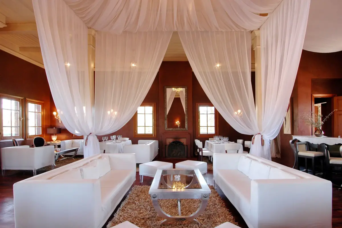Salon de restaurant à Marrakech avec voilages blancs, canapés et tables dressées pour un dîner