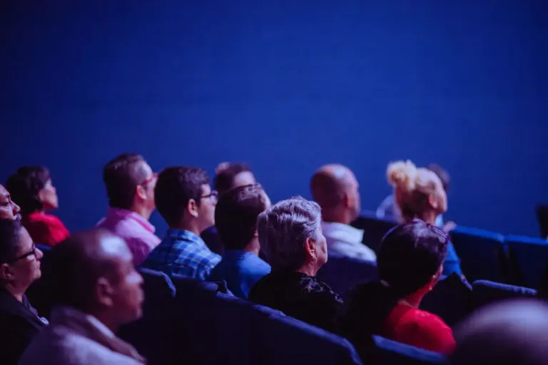 Public de conférence assis en rangs dans une salle plongée dans une lumière bleue