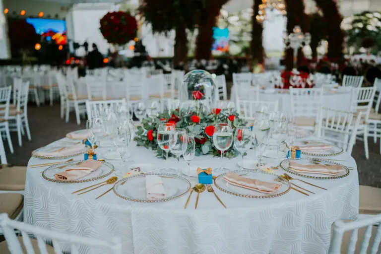 Table ronde dressée pour un dîner de réception, fleurs rouges, verres et assiettes dorées
