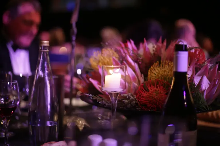 Table d'un dîner de gala éclairée à la bougie, bouquet de proteas et invités en tenue de soirée