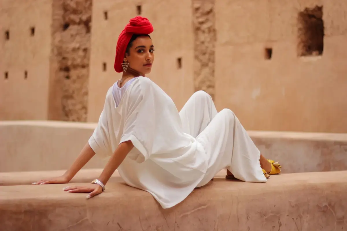 Femme en blanc qui pose sur un muret dans une cour de Marrakech, foulard rouge