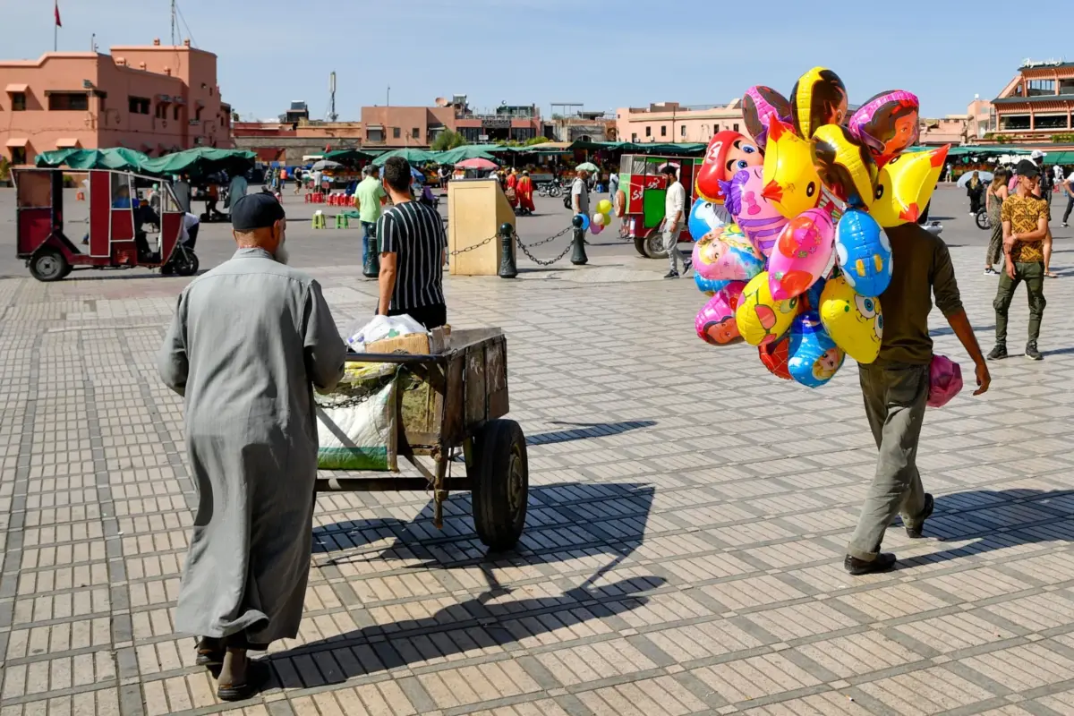 Place Jemaa el-Fna à Marrakech sous le soleil, avec un marchand de ballons et une charrette
