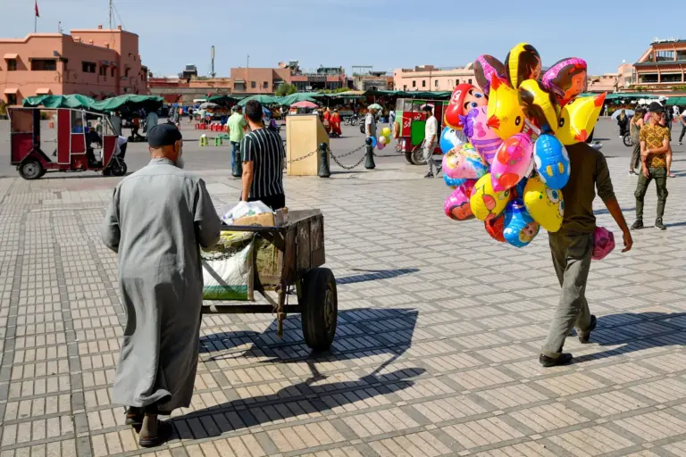 Place Jemaa el-Fna à Marrakech sous le soleil, avec un marchand de ballons et une charrette