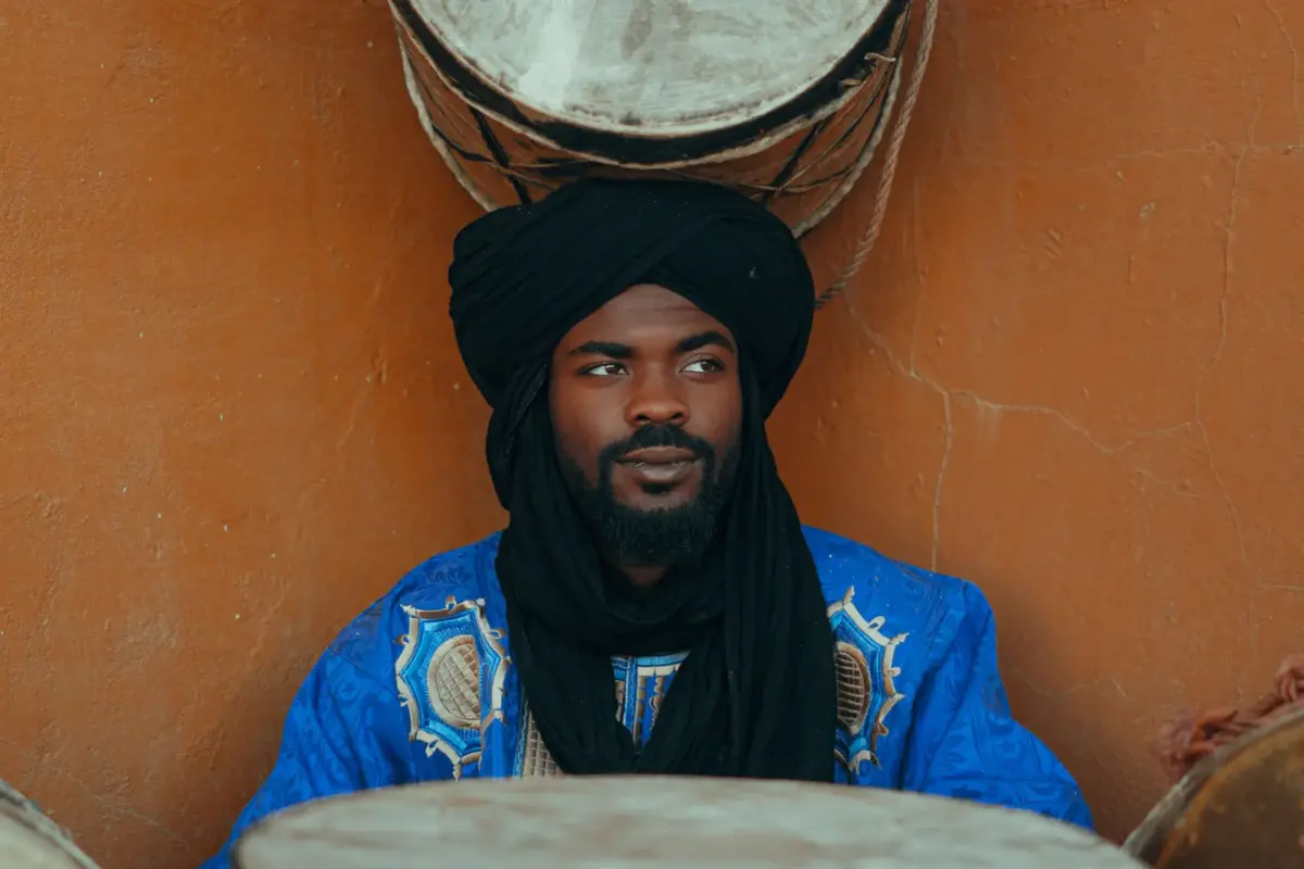 Musicien marocain en tenue traditionnelle et turban noir, entouré de tambours