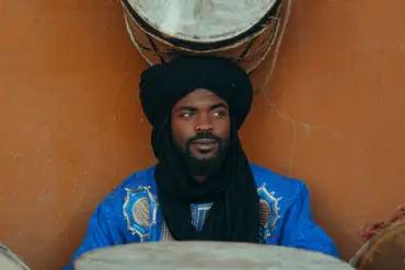 Musicien marocain en tenue traditionnelle et turban noir, entouré de tambours