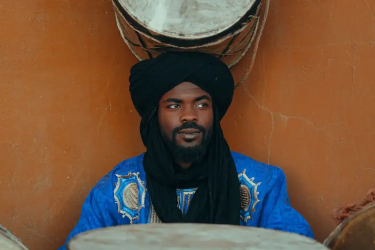 Musicien marocain en tenue traditionnelle et turban noir, entouré de tambours