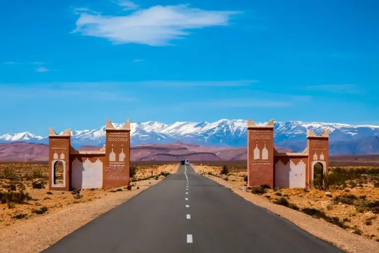 Route bordée de deux portes en pisé menant aux sommets enneigés de l'Atlas sous un ciel bleu d'hiver