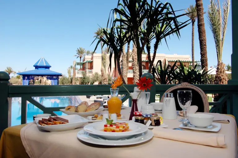 Petit-déjeuner servi en terrasse au bord de la piscine d'un hôtel de Marrakech, palmiers en fond