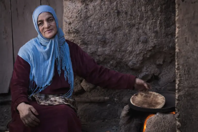 Cuisinière cuisant un pain plat sur un feu traditionnel dans la vallée de l’Ourika, près de Marrakech