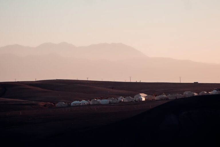 Camp de tentes blanches dans le désert d'Agafay au crépuscule, Atlas en fond
