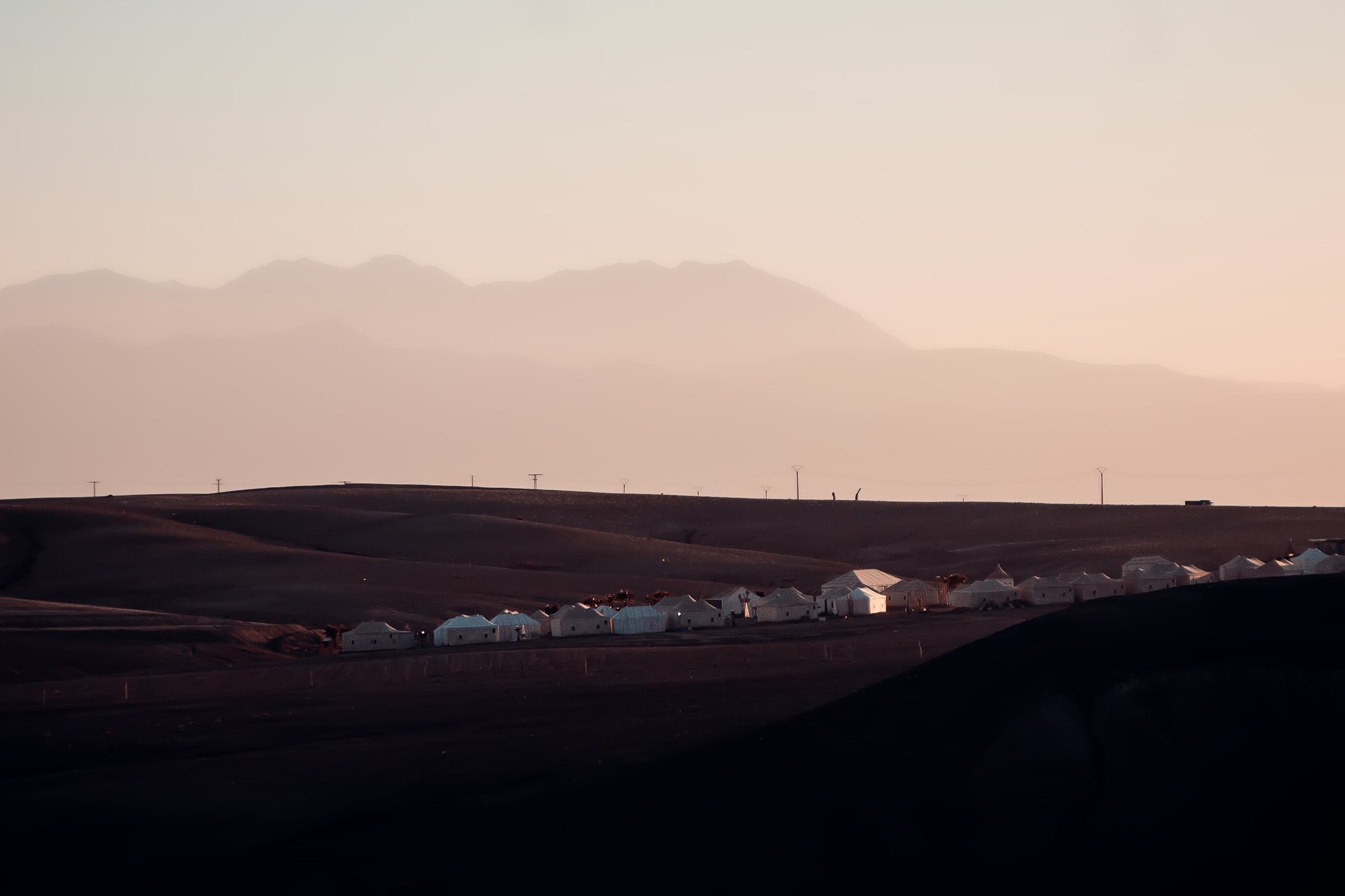 Camp de tentes blanches dans le désert d'Agafay au crépuscule, Atlas en fond