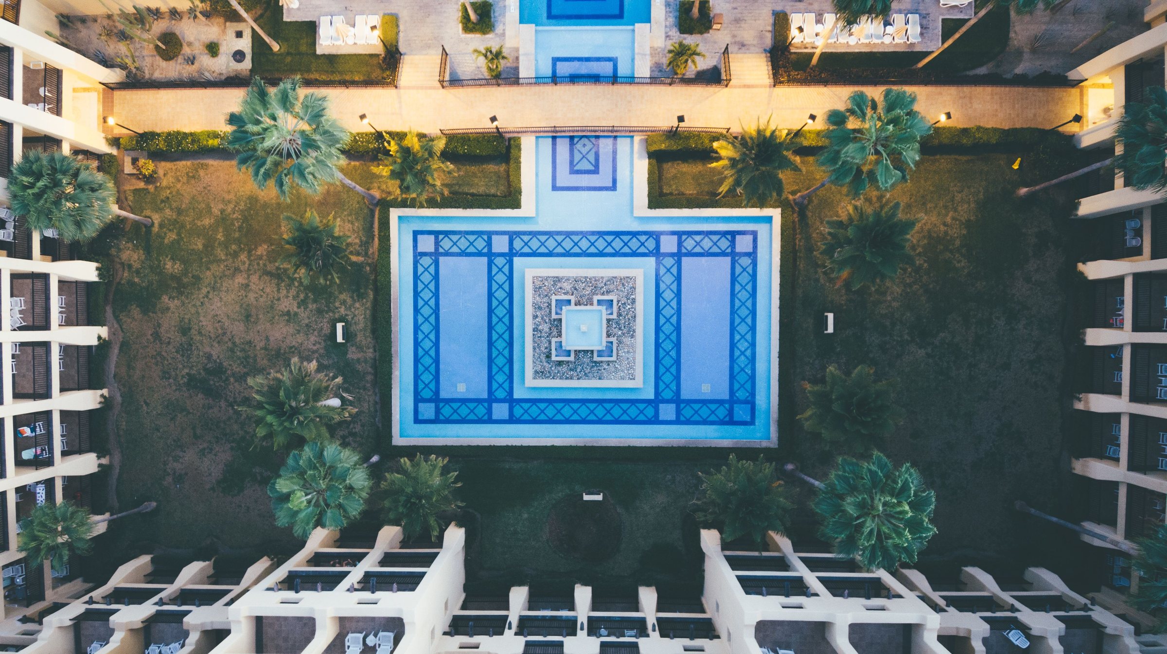 Vue aérienne d'un patio d'hôtel avec bassin en zellige bleu et palmiers