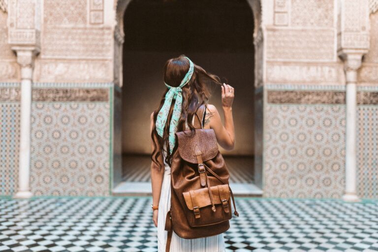 Femme avec sac à dos devant une arcade en zellige d'une médersa