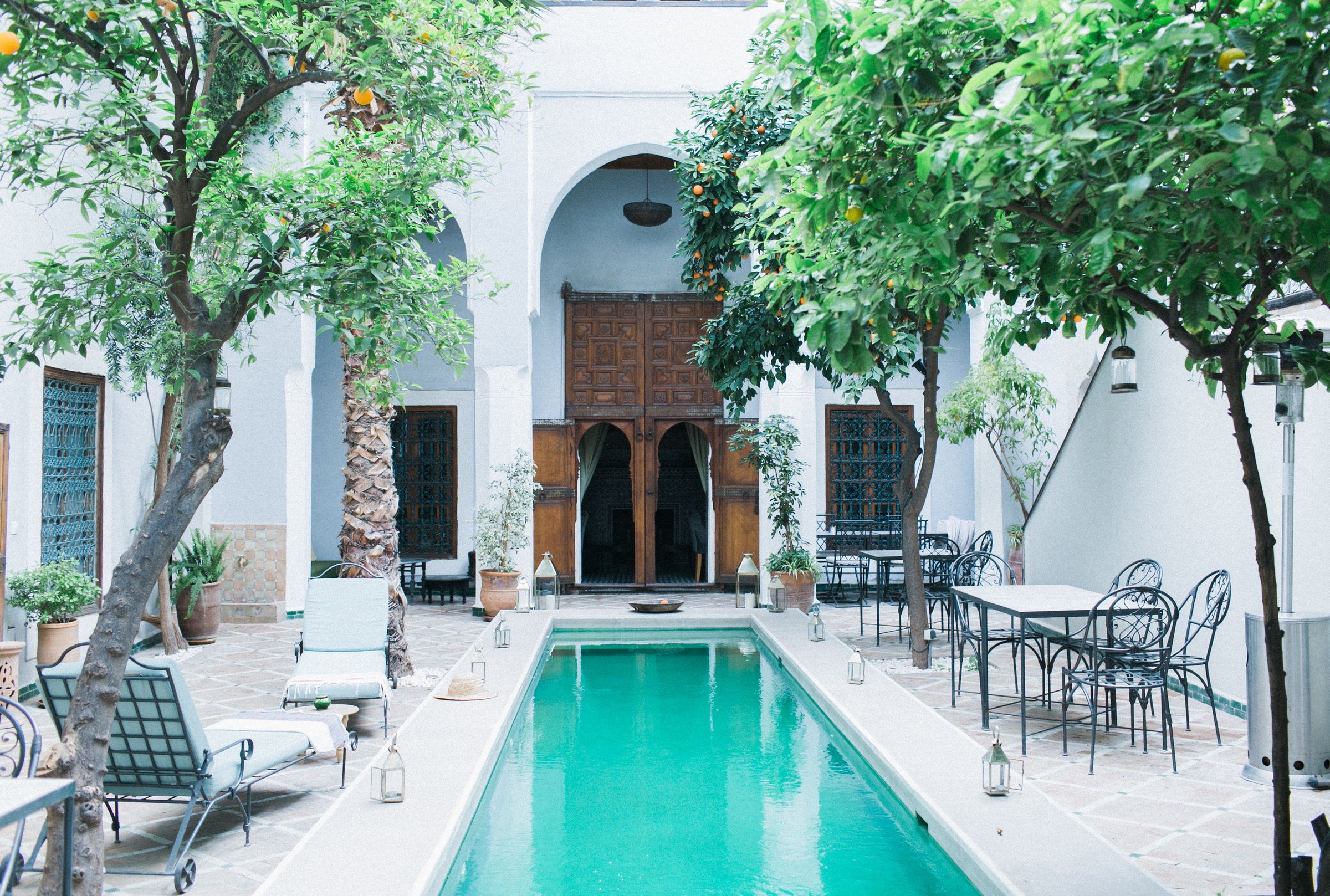 Patio de riad blanc avec piscine, orangers et tables en fer forgé
