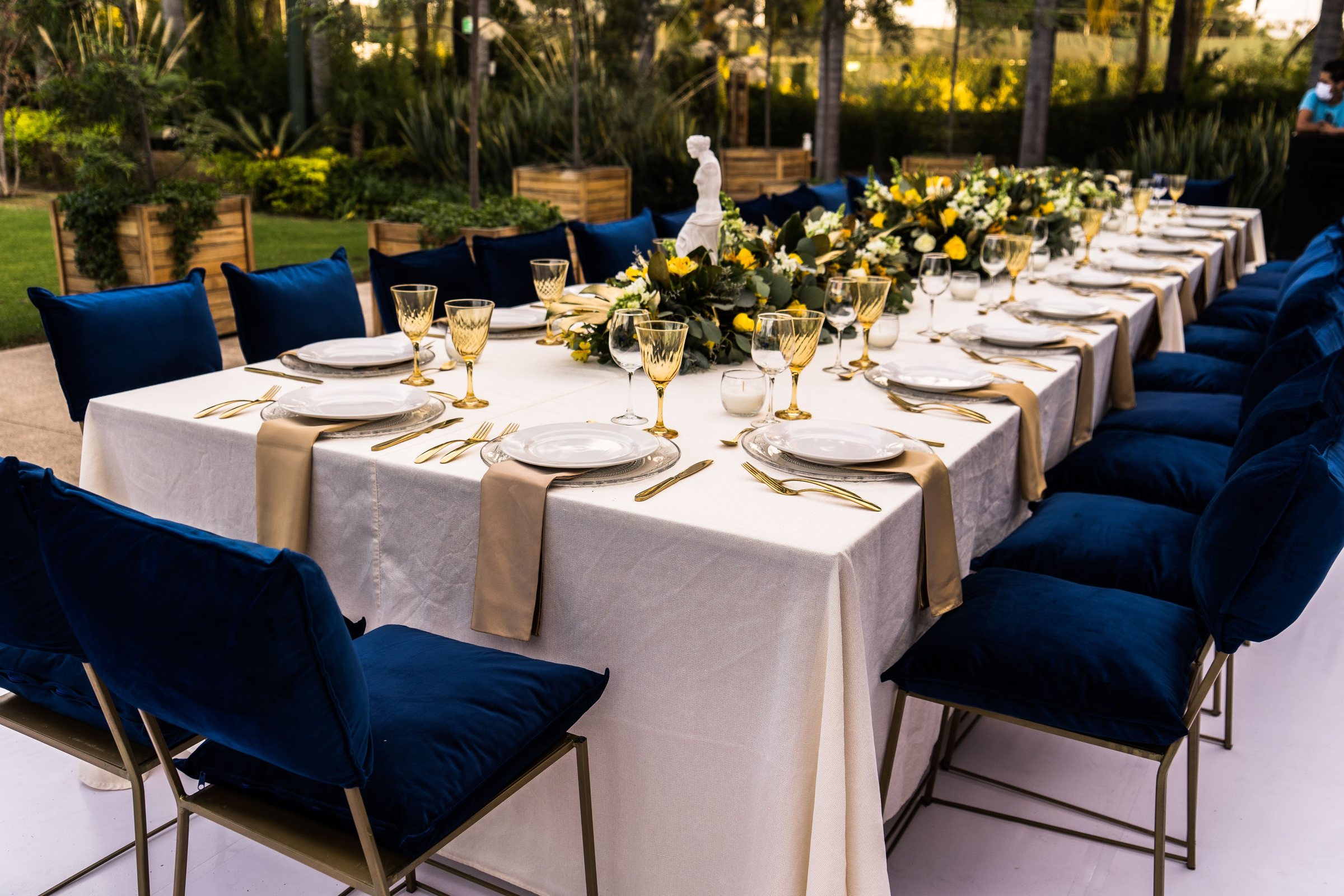 Longue table dressée en plein air, chaises en velours bleu et verres dorés