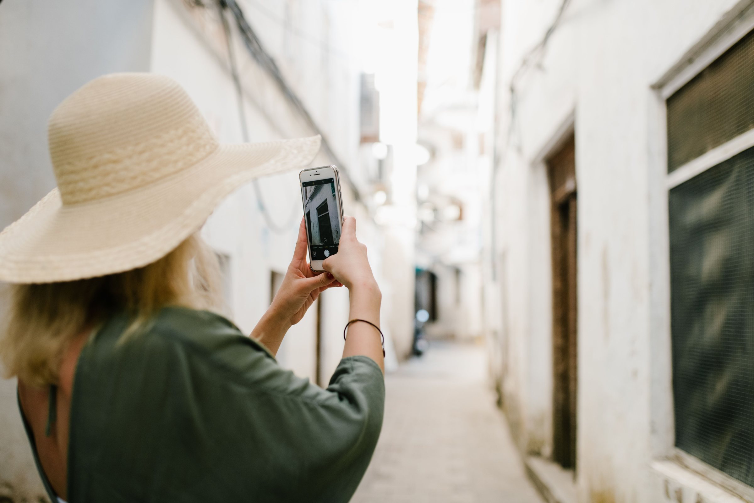 Voyageuse au chapeau photographiant une ruelle blanche avec son téléphone