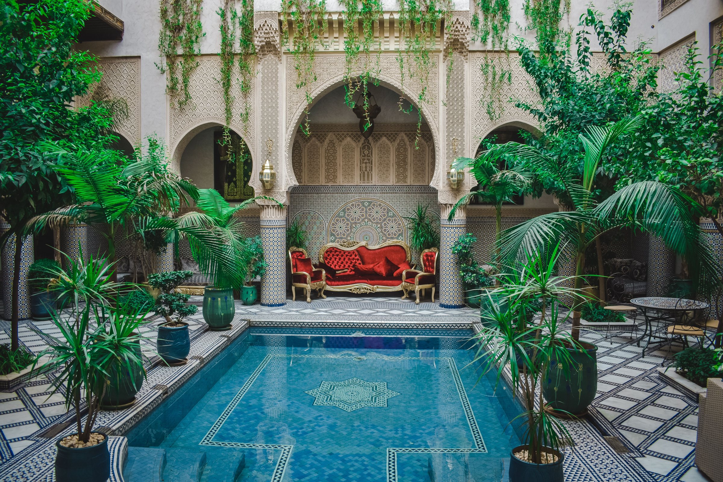 Patio de riad avec bassin en mosaïque, palmiers et arc sculpté