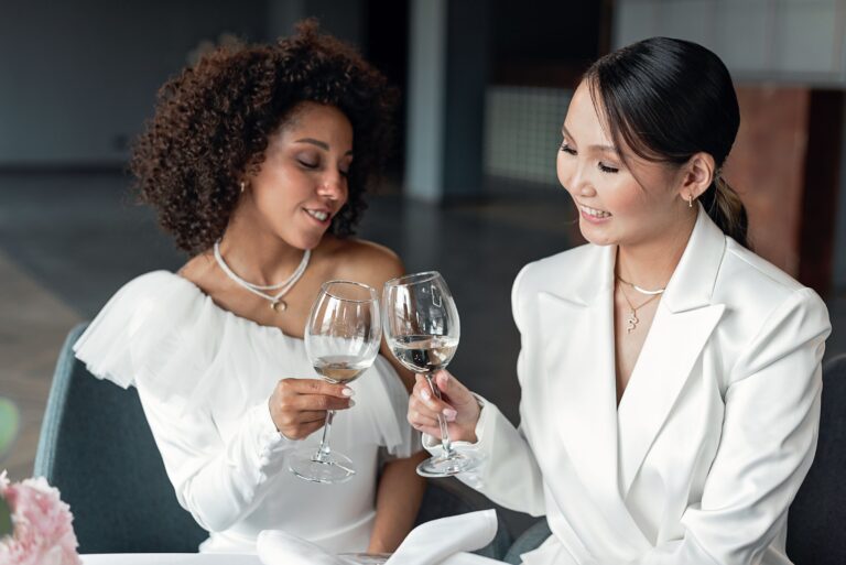 Deux mariées en blanc trinquent avec un verre de vin