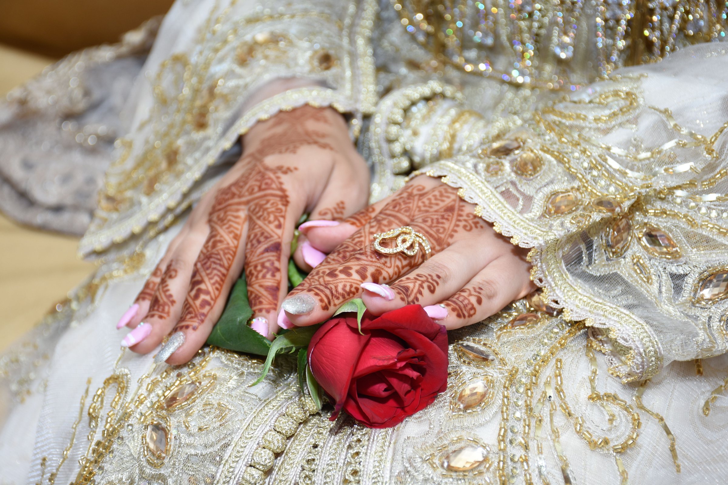Mains de mariée au henné en caftan brodé, tenant une rose rouge