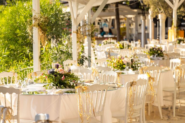 Réception en plein air, tables rondes, chaises blanches et fleurs sous une pergola