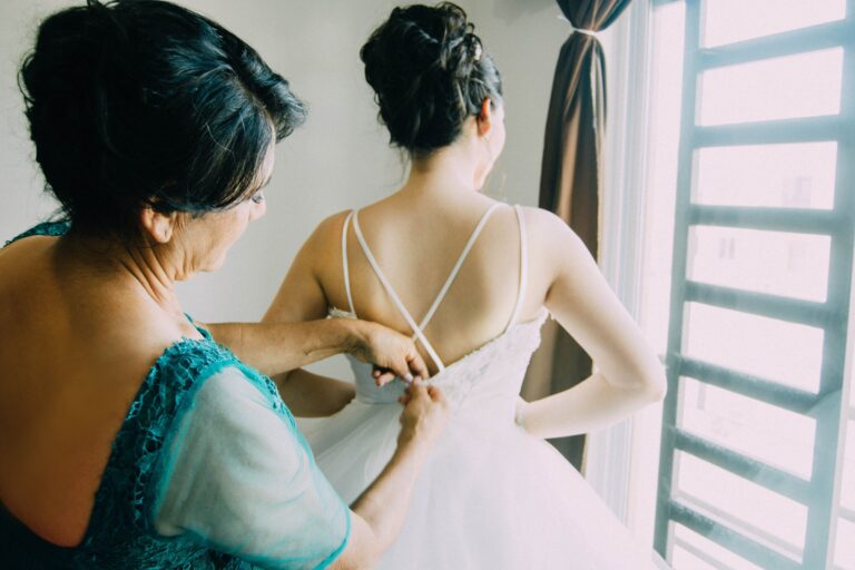 Une mère ajuste la robe de la mariée près d'une fenêtre