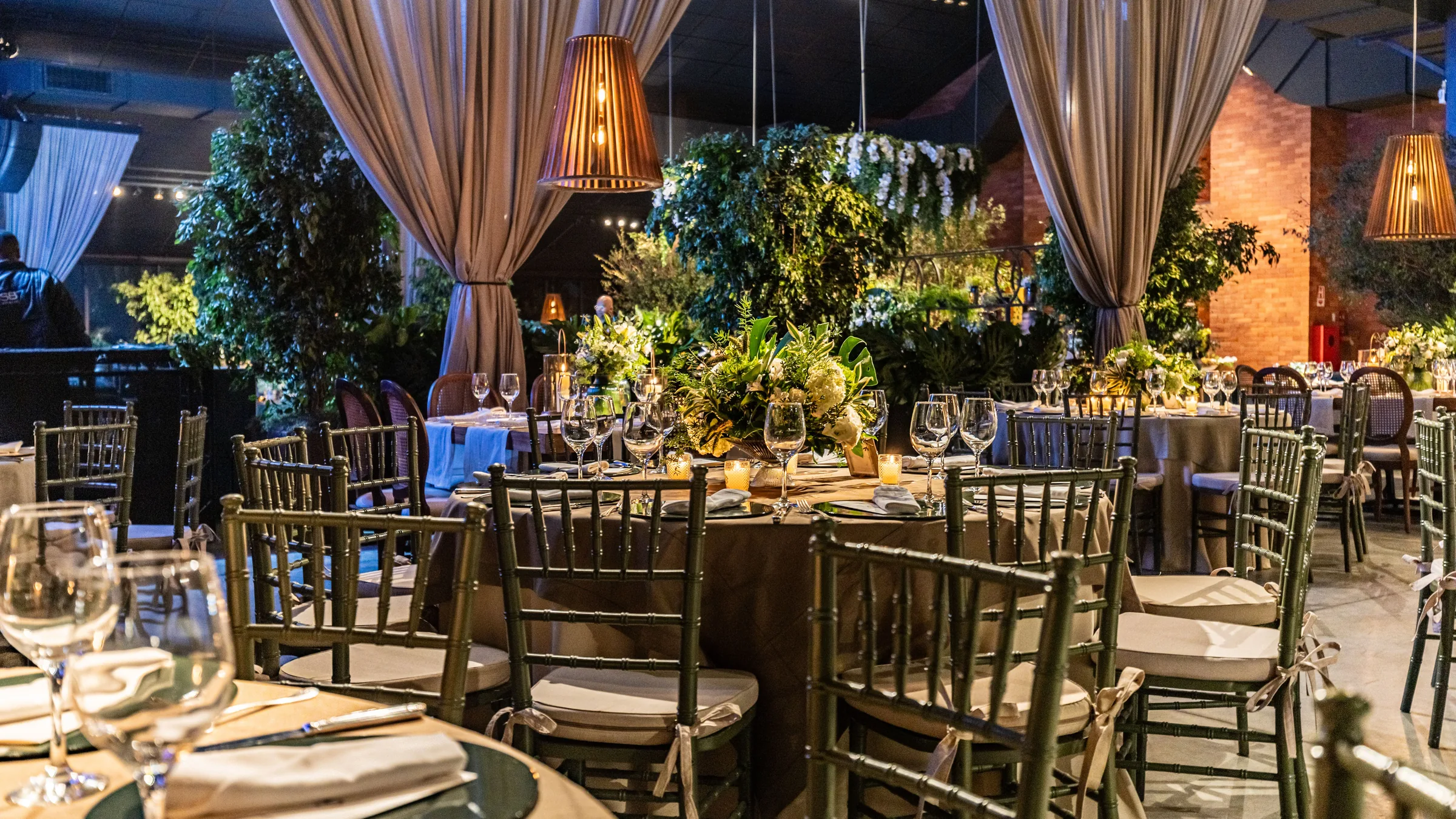 Grande table de mariage dressée aux bougies sous des guirlandes lumineuses